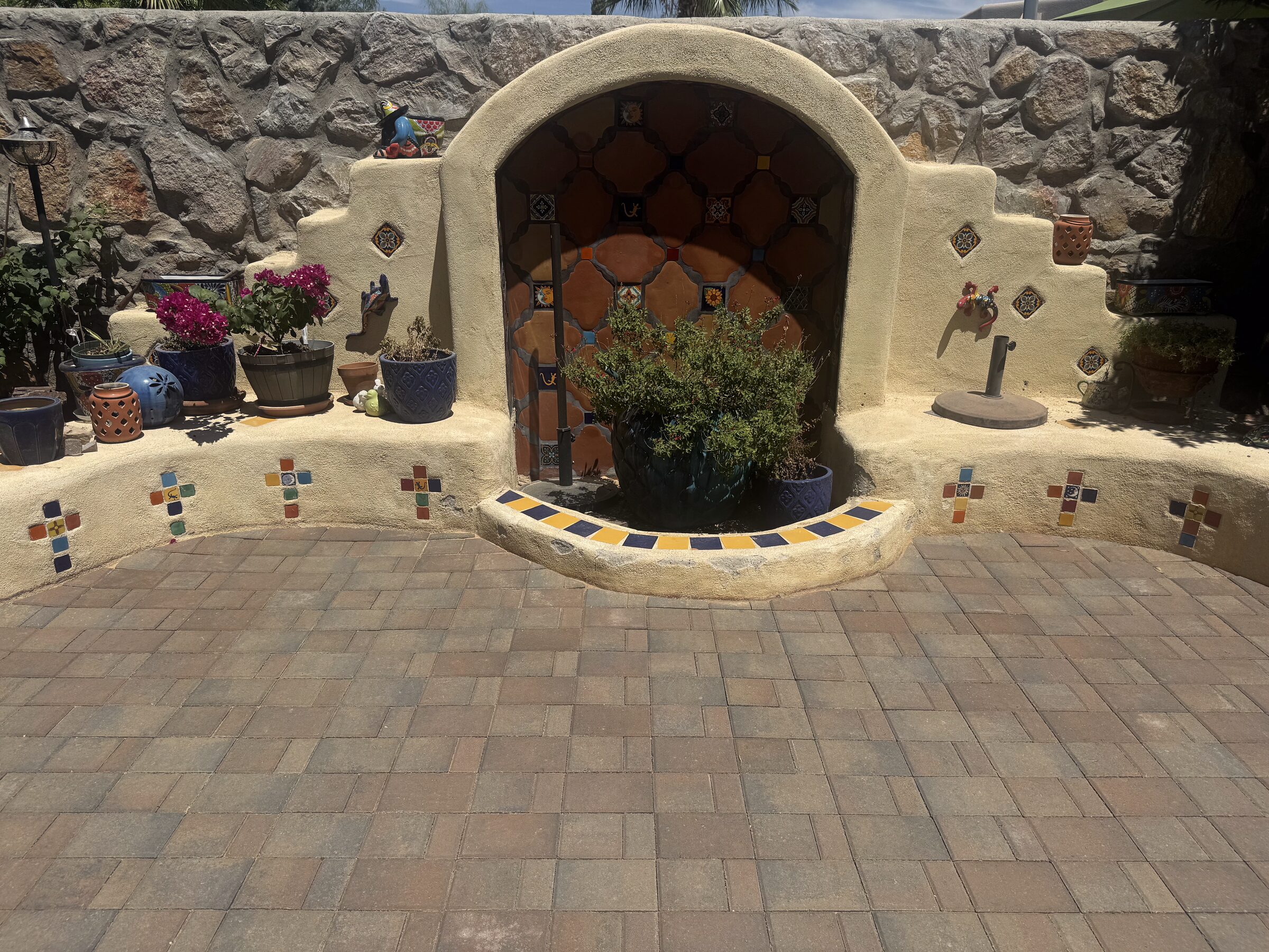 Interlocking pavers leading to a stucco arch wall with Talavera tile insets and colorful pottery in Las Cruces