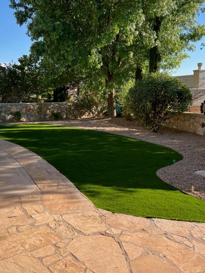 Artificial turf lawn with curved edges alongside flagstone patio and stone retaining wall