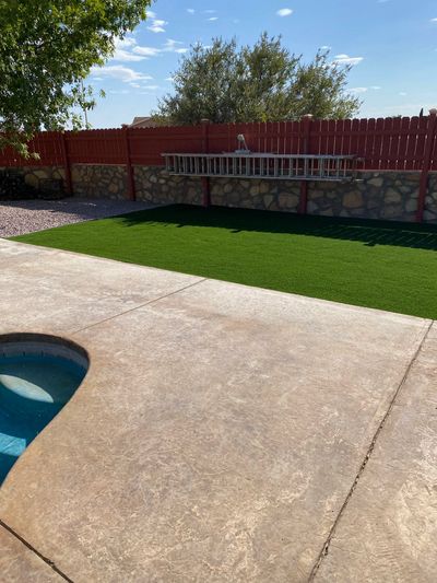 Artificial turf installed poolside with stone wall and stamped concrete patio