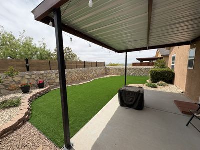 Artificial turf backyard with covered patio, stone retaining wall, and string lights