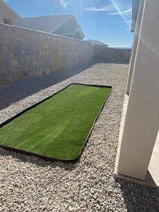 Compact artificial turf patch in a gravel courtyard between stone walls