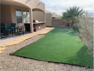 Artificial turf beside an outdoor kitchen with stone bar top and palm tree