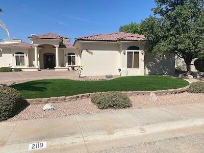 Front-yard artificial turf with stone border and mature trees at a Las Cruces residence