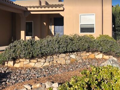 Front-yard xeriscape with trimmed hedges, natural stone border, and rock mulch