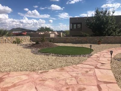 Flagstone pathway with artificial turf island, gravel beds, and stone wall backdrop