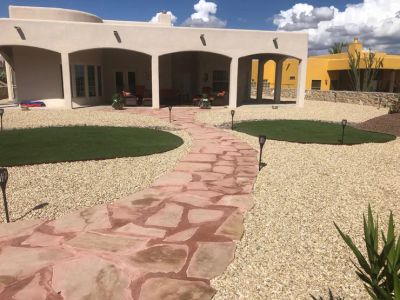 Flagstone walkway with solar lights leading to a southwest adobe home with artificial turf circles in gravel beds