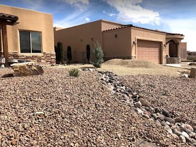 Adobe home with gravel yard, dry creek bed drainage, and iron gate entry
