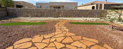 Flagstone walkway winding through red gravel beds with artificial turf accents and stone retaining wall