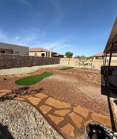 Backyard xeriscape with flagstone patio, turf circles, and dual-tone gravel against a stone wall