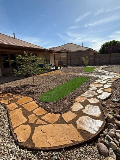 Backyard hardscape with flagstone patio, curving stone walkway, artificial turf strip, and gravel beds