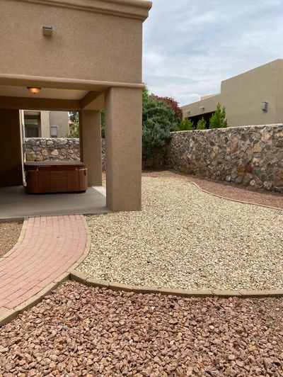 Brick paver border with dual-tone gravel and stone retaining wall around a covered patio