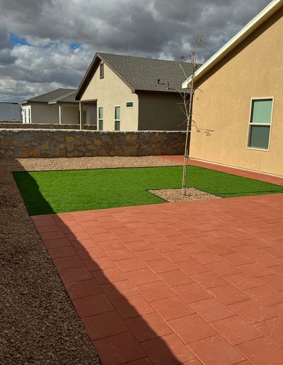 Red brick paver patio with artificial turf and young tree beside a stone wall