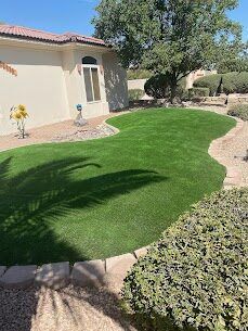 Front-yard artificial turf with established plantings and gravel border at a Las Cruces home