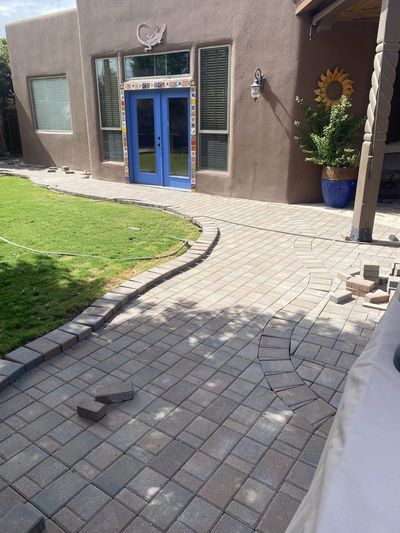 Paver walkway installation in progress at a southwestern adobe home with blue french doors and tile accents