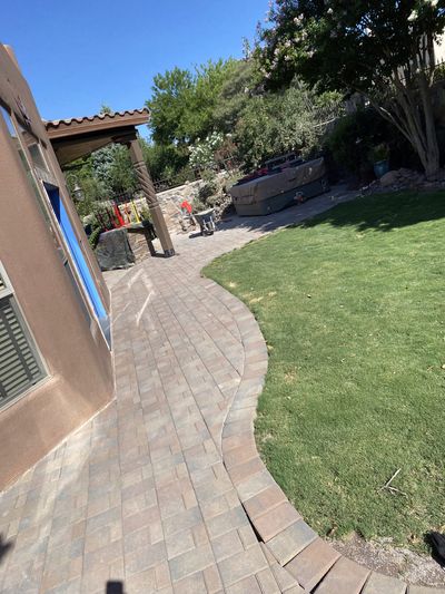 Curving brick paver walkway alongside green lawn leading to a covered patio and hot tub at a Las Cruces home