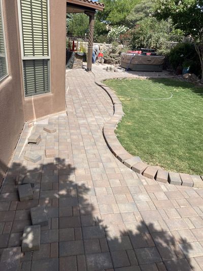 Curving brick paver patio being installed alongside green lawn with crew working in background