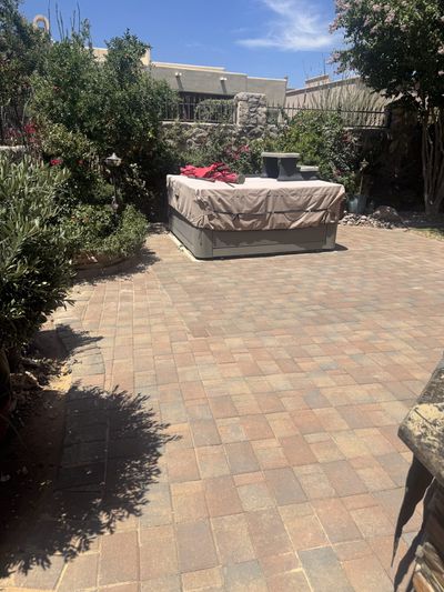Completed brick paver patio around a hot tub with mature landscaping and stone wall