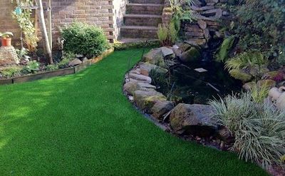 Stone-edged pond with waterfall feature and artificial turf walkway in University Park