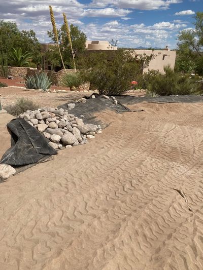 Landscape fabric and river rock being placed at the start of a drainage channel installation