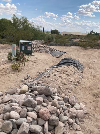 River rock drainage channel under construction running past a utility box in a desert yard