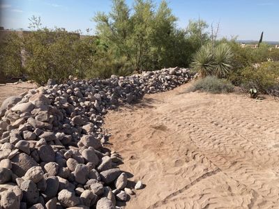 Nearly finished river rock drainage channel winding through desert landscaping in Las Cruces