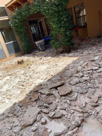 Old flagstone patio demolished into rubble around a fresh-cut tree stump in a Las Cruces courtyard