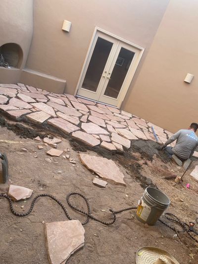 Stone mason setting flagstone in mortar near a kiva fireplace during a Las Cruces patio rebuild