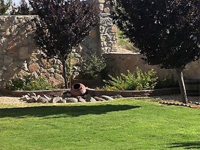 Shaded turf lawn with clay olla accent, rock border, and stone wall
