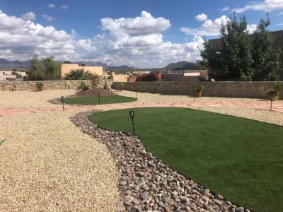 Backyard with artificial turf circles bordered by river rock in gravel beds with Organ Mountains in the background