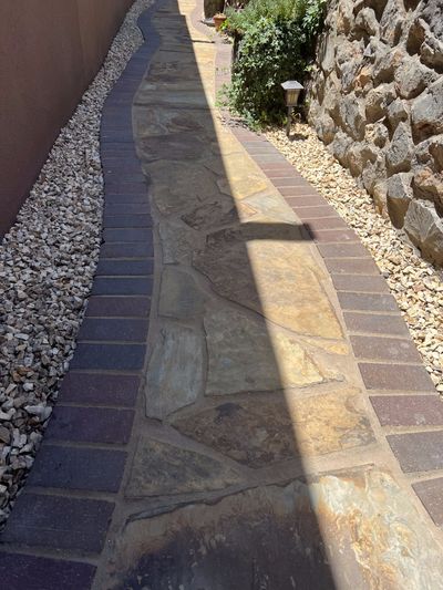 Flagstone walkway with brick paver border between gravel beds and natural rock wall