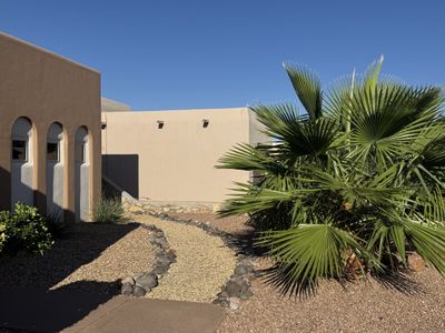Adobe home entry with stone-bordered gravel walkway and fan palm in a Las Cruces xeriscape